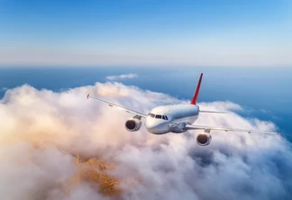 Passenger airplane flying over clouds at sunset. Landscape with big white airplane, low clouds, sea, blue sky in the evening. Aircraft is landing. Business trip. Commercial plane. Travel. Aerial view