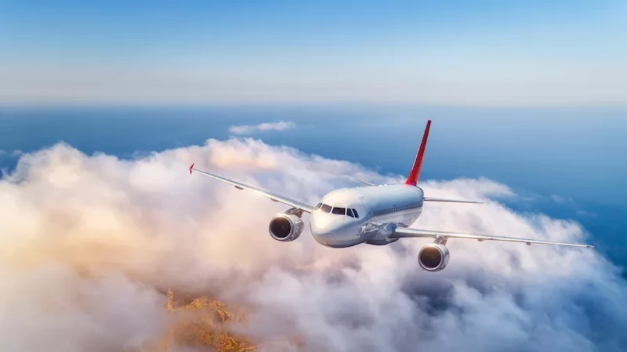 Passenger airplane flying over clouds at sunset. Landscape with big white airplane, low clouds, sea, blue sky in the evening. Aircraft is landing. Business trip. Commercial plane. Travel. Aerial view